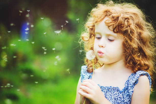 istock Curly girl blowing white dandelion in meadow. 874251048