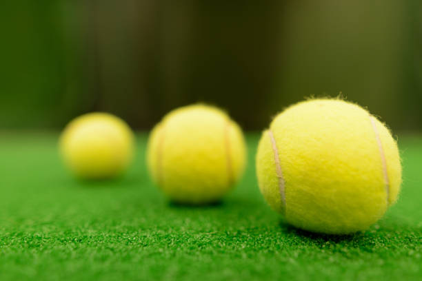 Yellow lawn tennis balls lie in close-up on a green background, tennis rackets are visible from the side. High quality photo