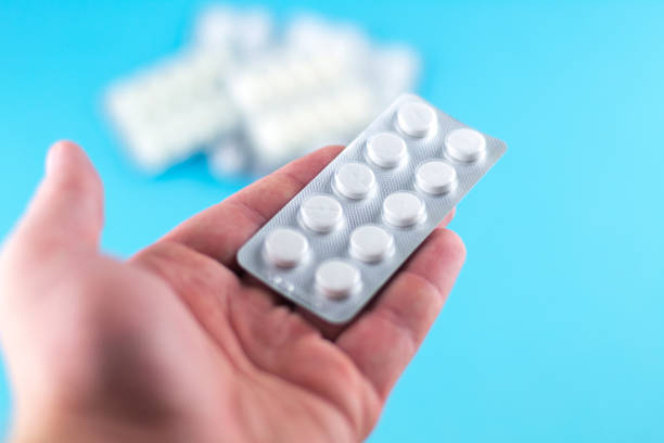 istock The man hand is holding a pack of white pills packed in blisters with copy space on blue background. Focus on foreground, soft bokeh 874270096
