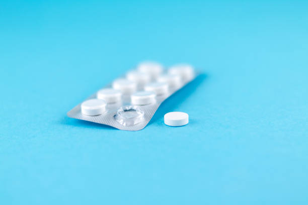 istock Packs of white pills packed in blisters with copy space on blue background. Focus on foreground, soft bokeh 874270330