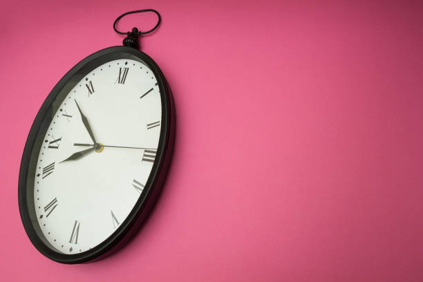 istock A clock with Roman numerals on a pink background. 874271460