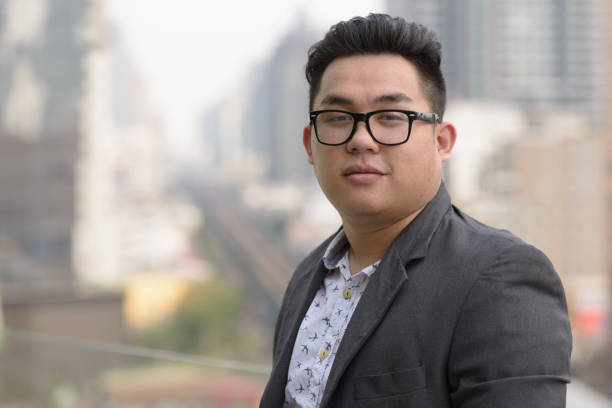 молодой красивый азиатский бизнесмен наслаждается жизнью в городе бангкок, таиланд - portrait human face men overweight стоковые фото и изображения