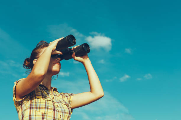 Beautiful Young Girl Looking Through Binoculars On Blue Sky Background. Travel Holidays Journey Concept stock photo