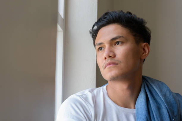 istock Young Asian man looking out through the window at home 874285118