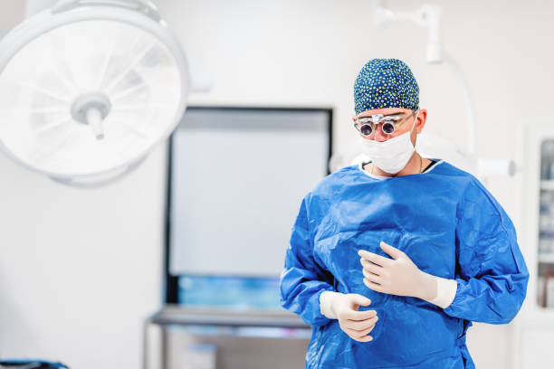 istock Cosmetic plastic surgeon wearing scrubs, goggles and gloves getting ready for surgery 874285672