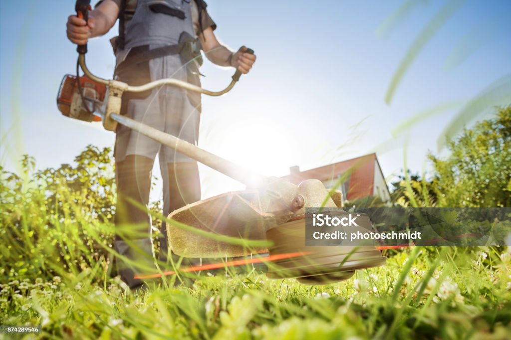 Gardening with a brushcutter Dramatic view of a brushcutter trimming grass. Mowing Stock Photo