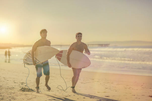 istock Male hispanic surfers running in the beach at sunset 874291316
