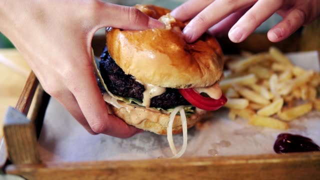 Female hands taking big tasty burger from a wooden tray and getting ready to eat it. Slowmotion shot