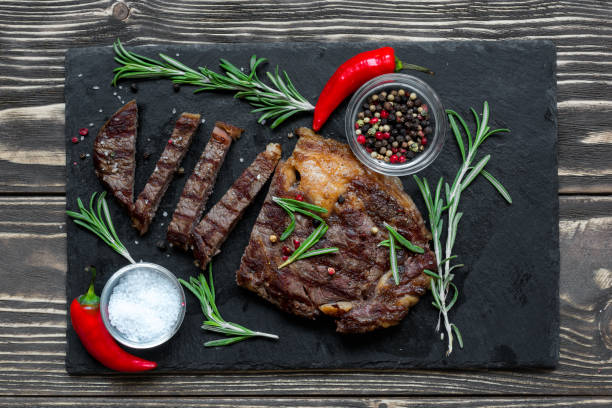istock Grilled beef steak with herbs and spices on black slate cutting board 874297822