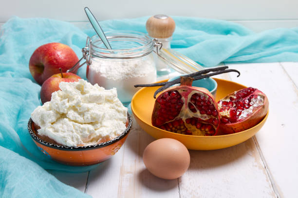 istock Cottage cheese, egg, sugar, salt, pomegranates, apples, flour and vanilla pods on a white table 874314358
