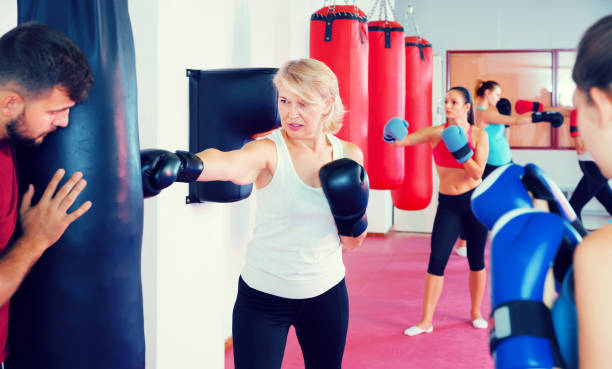 istock mature female is doing exercises with punching bag in gym 874314490
