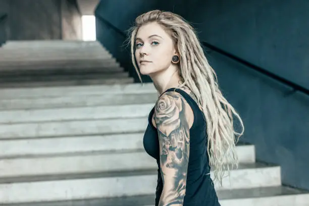 Portrait of young tattooed women with blond dreadlocks on urban staircase
