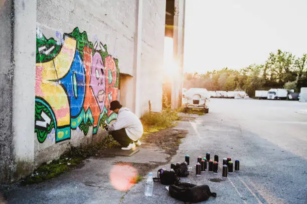 Young Man Doing Graffiti with Sunset Through the Building