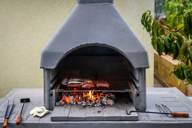 Barbecue in built barbecue grill fireplace with fish and chevaps. Concrete bbq fireplace  back yard fireplace in Croatia.