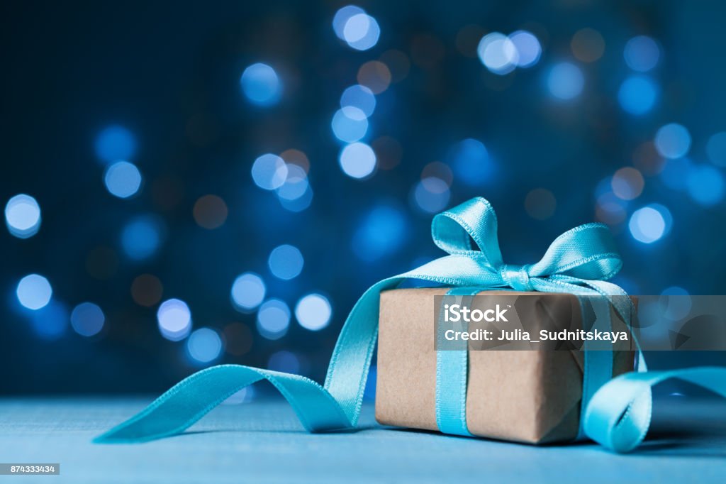 Christmas gift box or present with bow ribbon on magic blue bokeh background. Christmas gift box or present with bow ribbon on magic blue bokeh background. Copy space for greeting card. Blue Stock Photo
