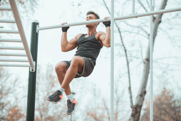Workout man with sports gloves doing chin-ups An attractive young man with sports gloves is seen doing chin-ups. chin ups photos stock pictures, royalty-free photos & images