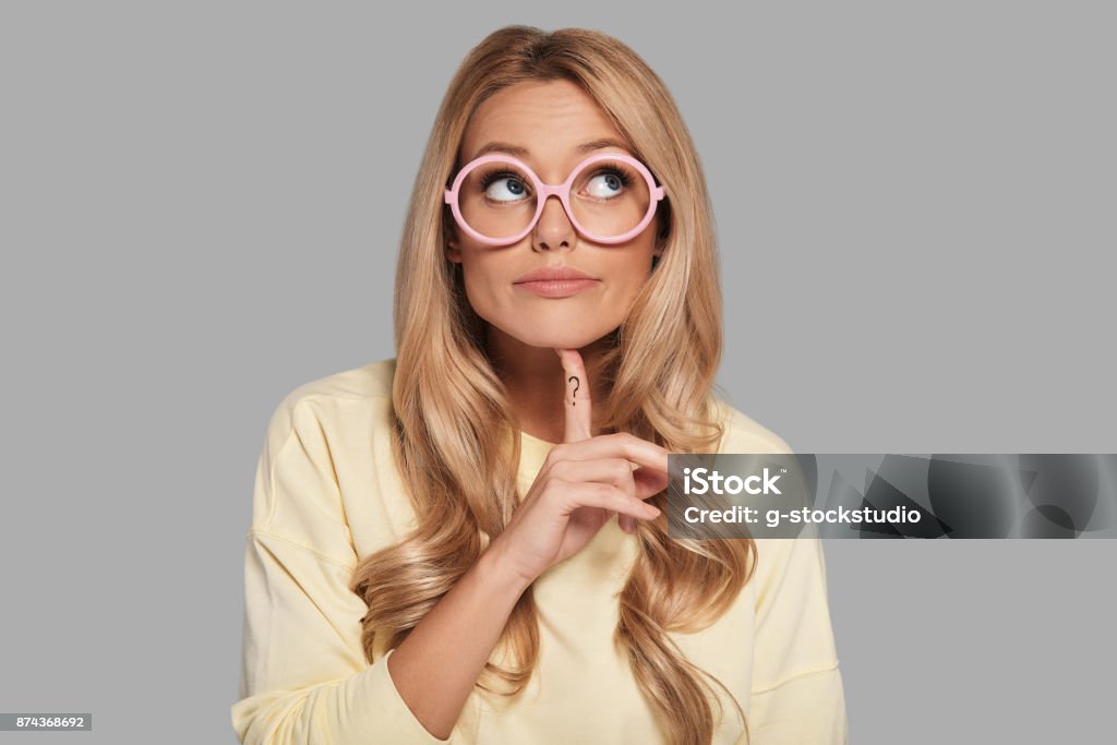 Searching for inspiration. Confused young woman looking away and gesturing while standing against grey background Women Stock Photo