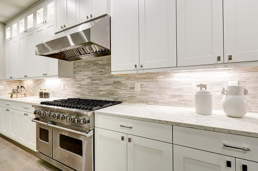 Gourmet kitchen features white shaker cabinets with marble countertops paired with stone subway tile backsplash and stainless steel hood over eight burner gas range. Northwest, USA
