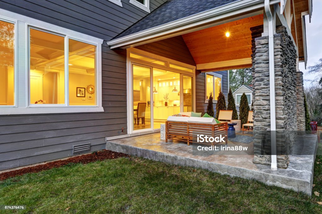 Chic covered back patio with stone wall Chic covered back patio with built in gas fireplace, stone pillars, plank vaulted ceiling over cozy teak wood sofa set topped with white cushions and green pillows. Northwest, USA Porch Stock Photo