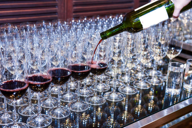Pouring red wine from bottle into the wineglass on row of glasses