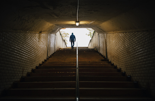 Anonymous man walking up the stairs in an old tunnel in a park.