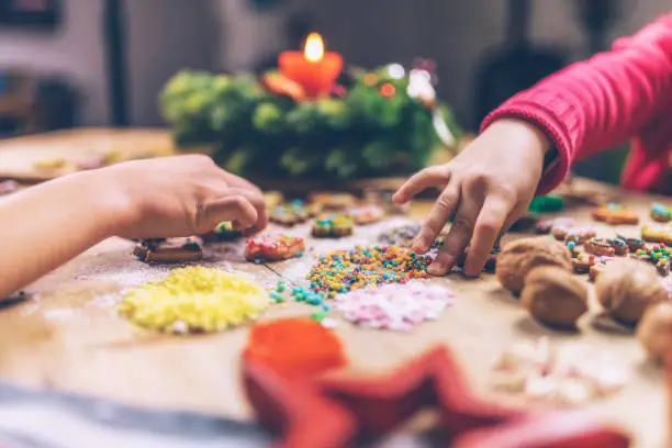 view on kids hands decorating christmas cookies together on rustic wooden table