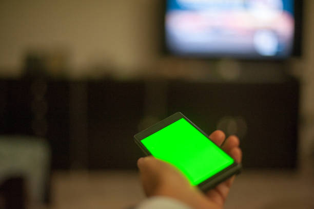 istock Female Hand Holding Smart Phone with Green Screen at Home 874403192