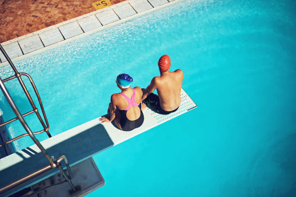 Taking it all in High angle shot of two young swimmers sitting on a diving board women exercising swimming pool young women stock pictures, royalty-free photos & images