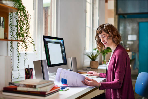 Sorting out some admin for her home-based business Shot of a young woman working on a computer in her home office paper based equipment stock pictures, royalty-free photos & images