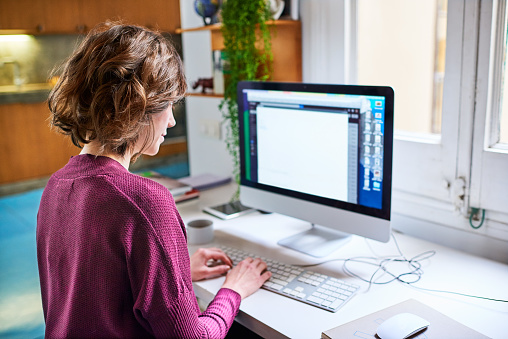 Rearview shot of a young woman working on a computer in her home office