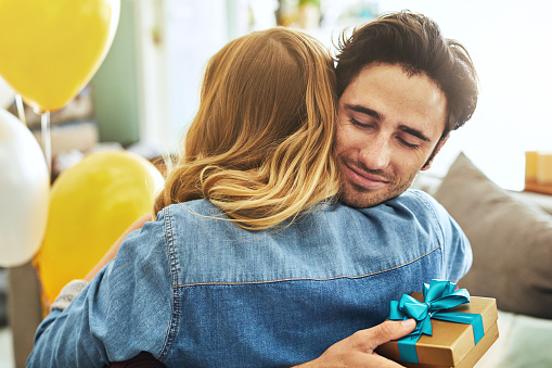 Shot of a cheerful young man hugging his girlfriend after receiving a gift from her at home