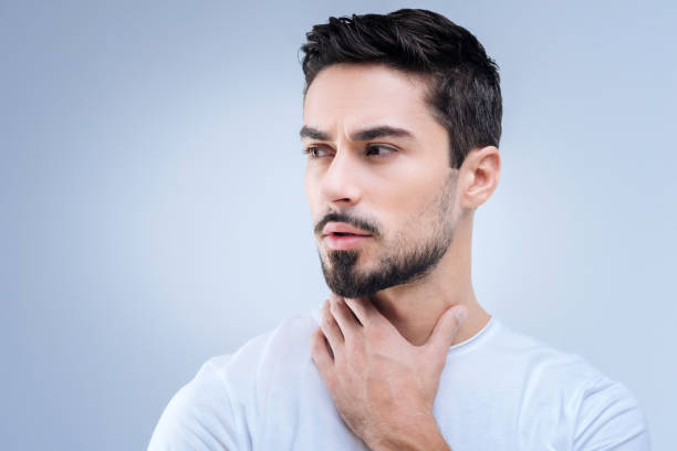 istock Serious young man looking worried while touching his neck 874426378