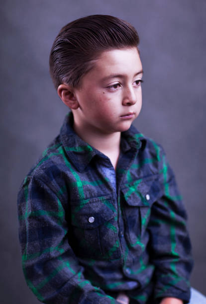 Handsome little boy with greased pompadour rockabilly hairstyle wearing a green flannel wool shirt with western pearl snaps Handsome mixed race Asian Caucasian little boy with a serious expression on his face with greased pompadour rockabilly hairstyle wearing a green flannel cowboy wool shirt with western pearl snaps in front of a grey background wall rockabilly boys stock pictures, royalty-free photos & images