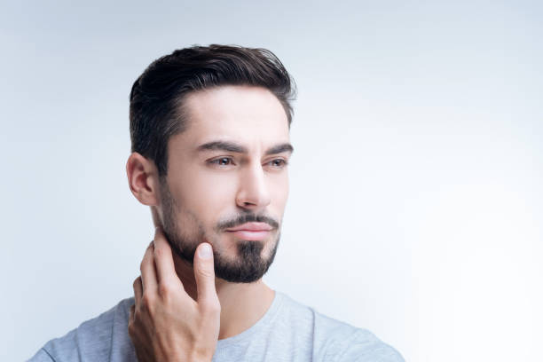 Thoughtful young man touching his neck while looking into the distance