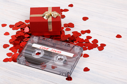 Audio cassette tape with present box, label text love songs on wooden background.