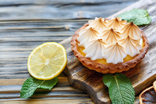 Tartlet with Italian meringue and lemon cream on a wooden stand, selective focus.