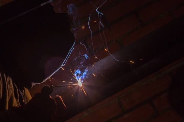 istock Welding of pipes to workers in a mask on a dark background. 874460848