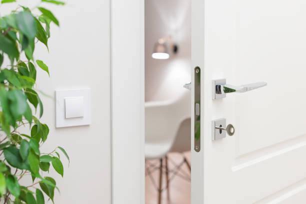 Close-up elements of the interior of the apartment. Ajar white door Close-up elements of the interior of the apartment. Ajar white door. Chrome door handle and lock with key. The light switch on the wall ajar stock pictures, royalty-free photos & images