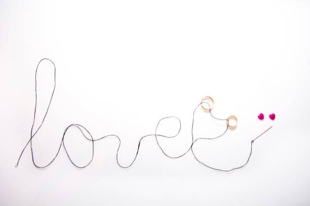 istock word love written with black thread and the needle inserted two gold wedding bands, there are two pink hearts and white background 874482470