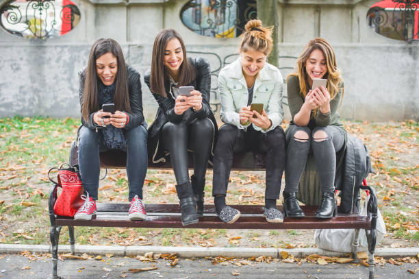 istock Happy four friends using cellphones on park bench 874486418