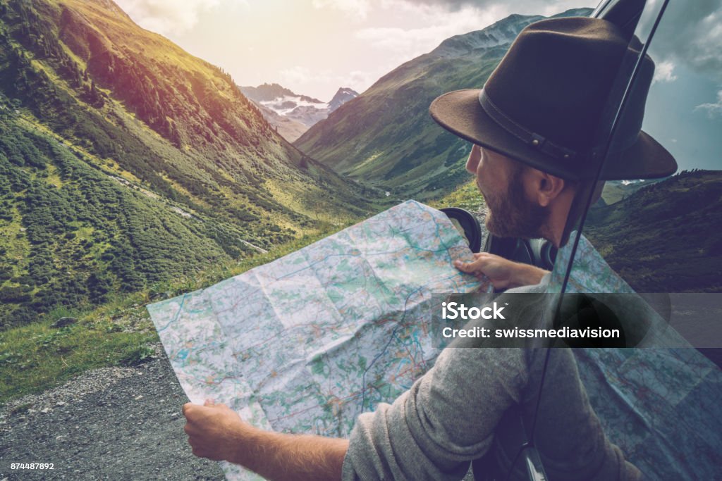 Young man looks at road map near on mountain road, Switzerland Young man in car on mountain road looks at map for directions. Mountain landscape in Summer, shot in Graubunden Canton, Switzerland. Road Map Stock Photo