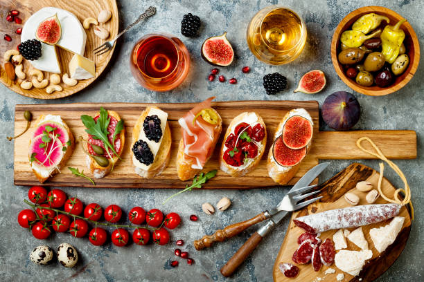 istock Appetizers table with italian antipasti snacks and wine in glasses. Brushetta or authentic traditional spanish tapas set, cheese variety board over grey concrete background. Top view, flat lay 874502884