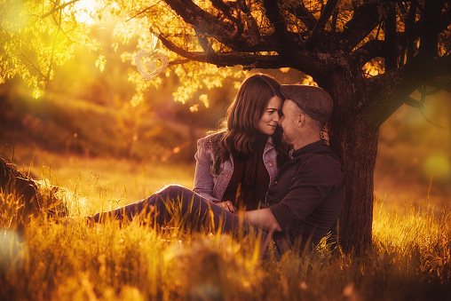 Love couple sitting under a tree in the colorful spring garden at sunset