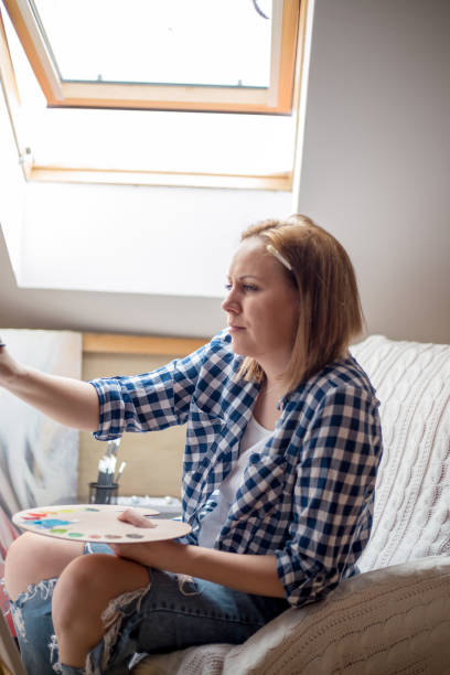 istock Happy young woman paints on canvas 874519414