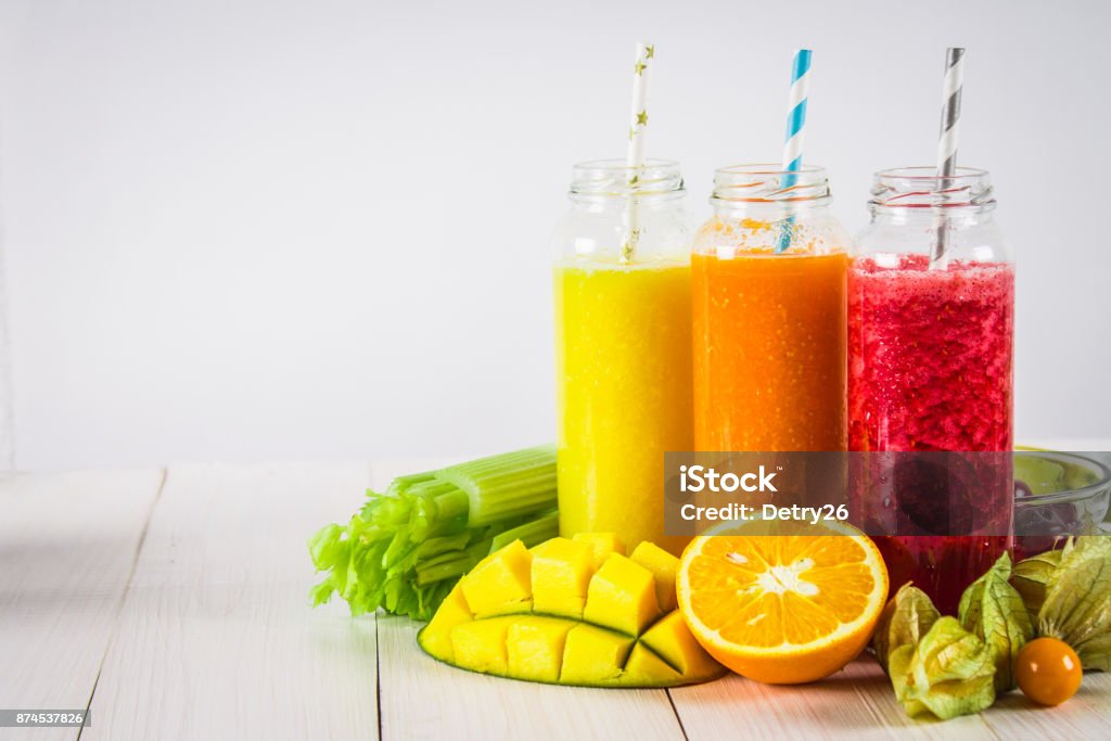 Multicolored smoothies in bottles of mango, orange, banana, celery, berries, on a wooden table. Multicolored smoothies in bottles of mango, orange, banana, celery, berries, on a wooden table Detox Stock Photo