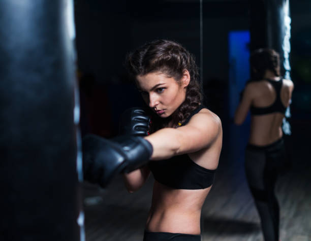 istock Young fighter boxer girl in training with heavy punching bag 874544450