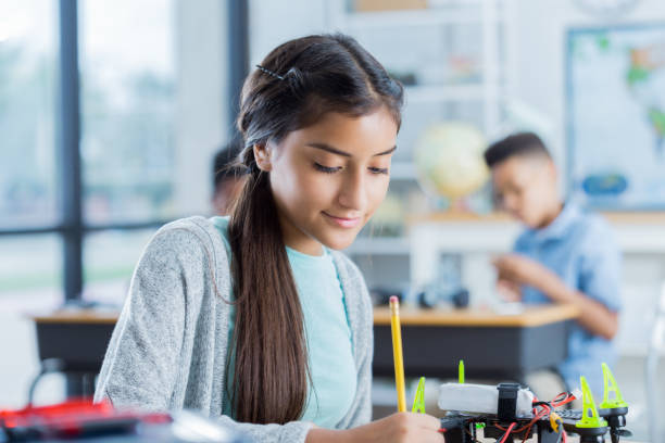 istock Confident Hispanic preteen girl works on project during technology class 874565214
