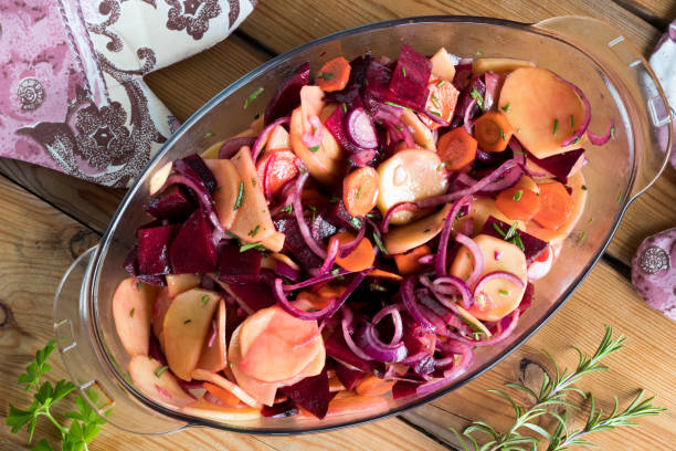 Sliced vegetables in a glass roasting pan on a table, ready to be baked in the oven. Top view.