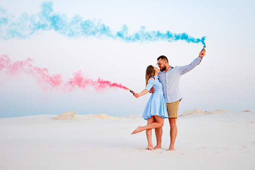 young couple kissing and holding colored smoke in hands, romantic couple with blue color and red color smoke bomb on beach