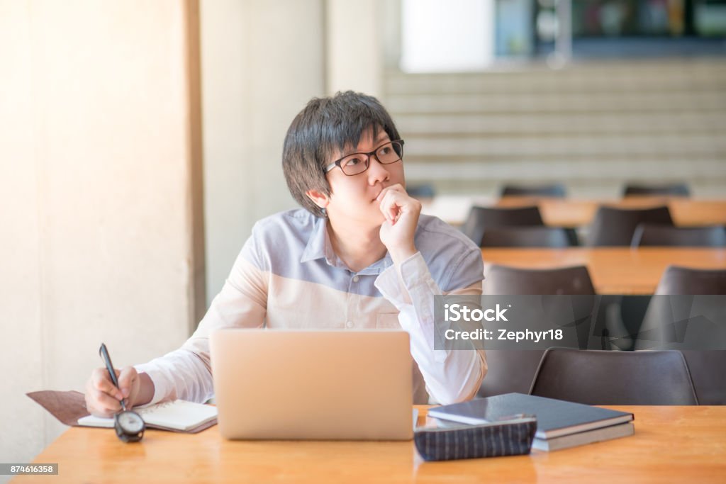 Young Asian man working with laptop and notebook in university Young Asian man writing on notebook and working with laptop computer in college building. high school or university student, educational concepts High School Student Stock Photo